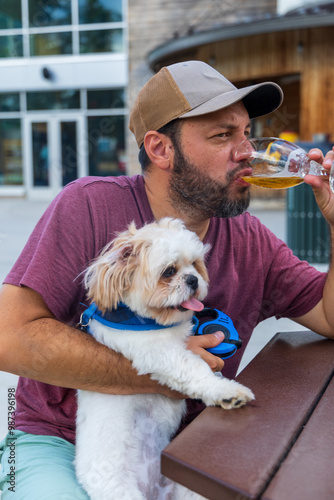 A man is sitting at a table with a dog and drinking a glass of beer