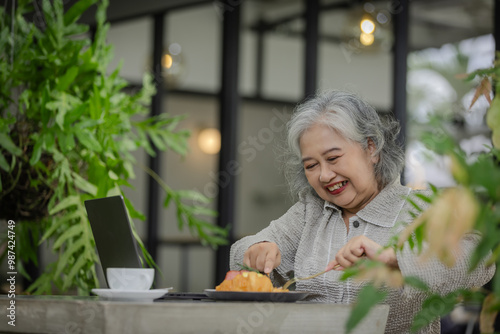 Elderly Woman Enjoying a Meal Outdoors with a Laptop, Surrounded by Lush Greenery and Natural Light photo