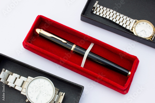 This high-quality image features a silver wristwatch placed on a clean white background, accompanied by a ballpoint pen. The minimalist setup highlights the watch's sleek design and the subtle contras photo