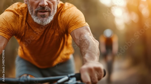 A close-up of a cyclist in an orange shirt riding a mountain bike on a forest path, with warm sunlight streaming through the trees, highlighting the effort.