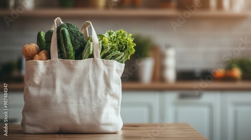 A cotton tote bag brimming with fresh vegetables like potatoes, broccoli, zucchinis, and greens sits on a wooden table in a modern kitchen setting, evoking sustainability and health. photo