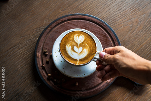 My hand holding a latte art cup with a heart pattern and coffee beans in the morning.
