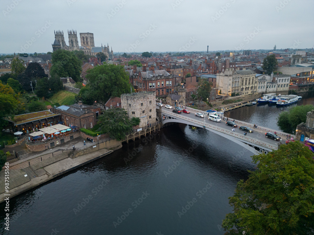 Obraz premium Historic Lendal Tower and Lendal bridge with traffic in York, UK at dusk. Aerial view towards Cathedral. Arch of the bridge with reflection in River Ouse. Waterfront with river cruise boats mooring.