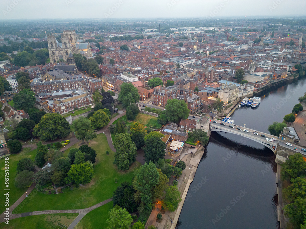 Fototapeta premium Aerial view of York city at dusk. Side view of Lendal bridge over river Ouse. Cars with lights crossing the bridge. Panoramic view of the historic city with Cathedral and Museum gardens.
