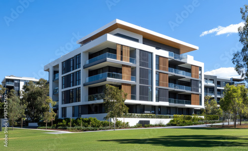 A modern apartment building with sleek architecture, featuring a white and grey exterior, glass windows, and wooden accents on the balconies, surrounded by green grass under a blue sky