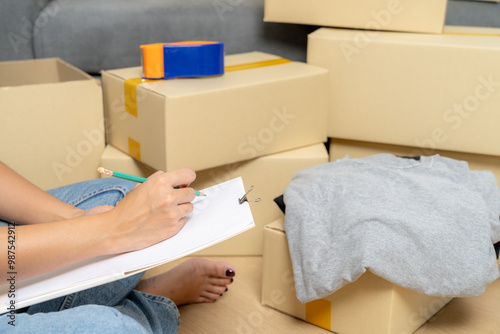 A young woman is packing clothes and belongings into boxes in preparation for moving into her new home