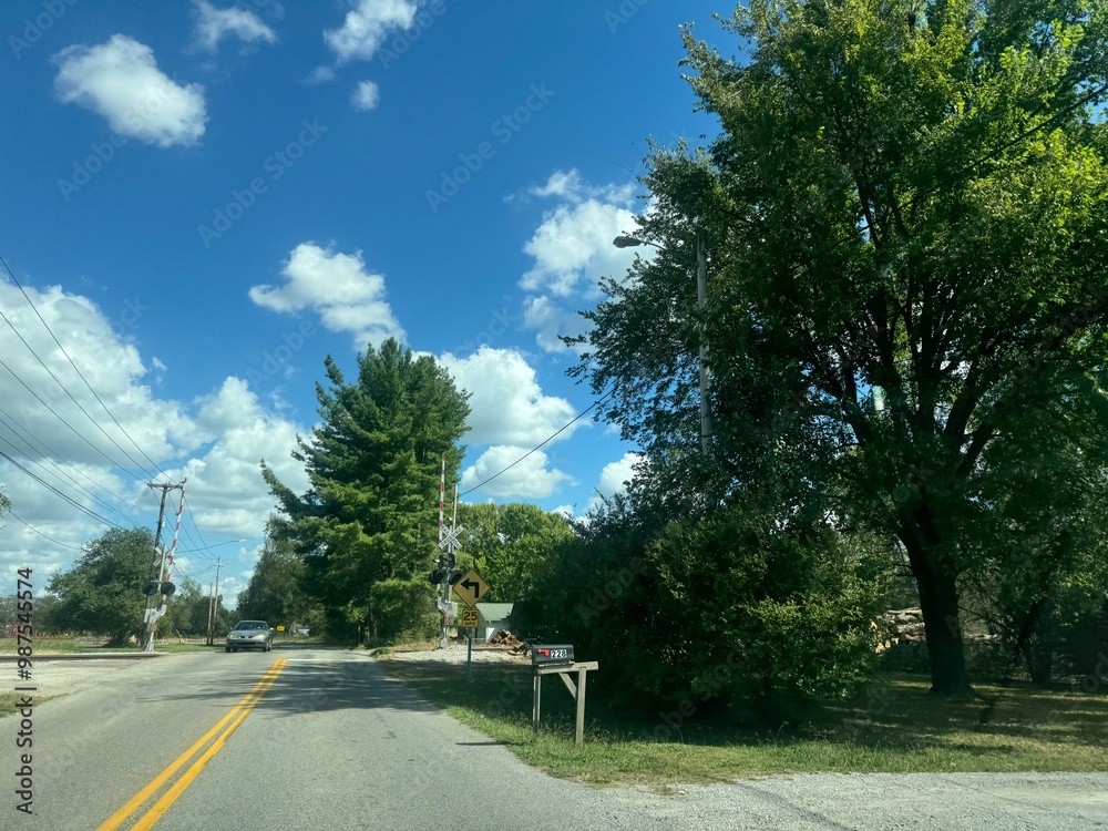 A quiet suburban road with lush trees and fluffy clouds on a sunny afternoon near a small town in autumn A quiet suburban road with lush trees and fluffy clouds on a sunny afternoon near a small town in autumn