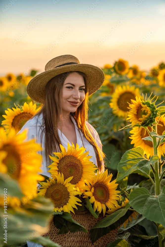 Φωτογραφία A girl in a hat on a beautiful field of sunflowers against the sky in the evening light of a summer sunset