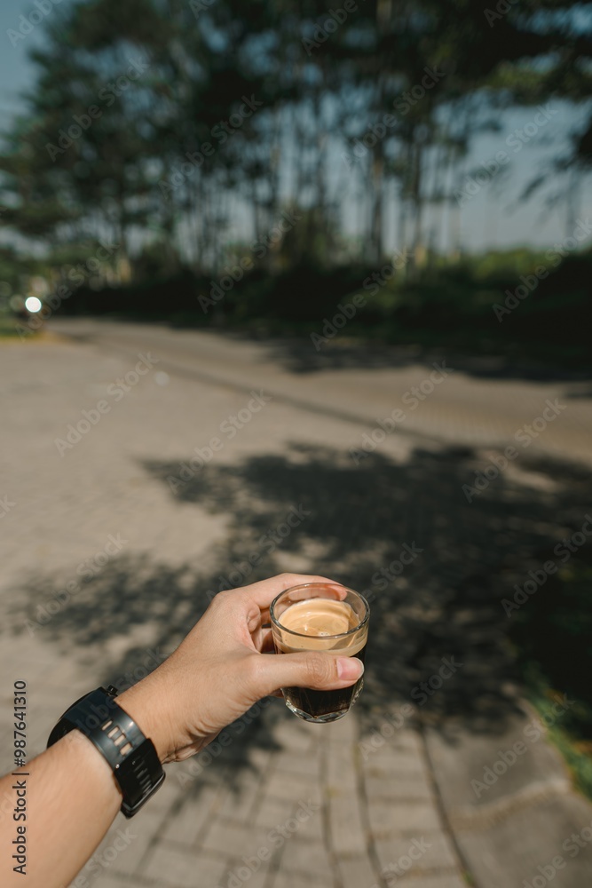 A hand holding a glass of single-shot espresso in the morning on the paved sidewalk street A hand holding a glass of single-shot espresso in the morning on the paved sidewalk street