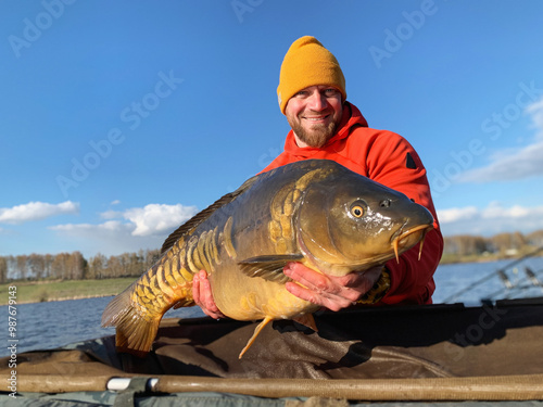 Fotografía A contented man holds a large carp caught from a lake in his hands, sport fishin