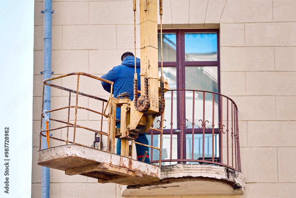 Worker on lifting platform repair damaged balcony of an old historic building. Restoration and renovation work, Damaged balcony floor, cracked concrete and plaster, rusty bars and reinforcement.