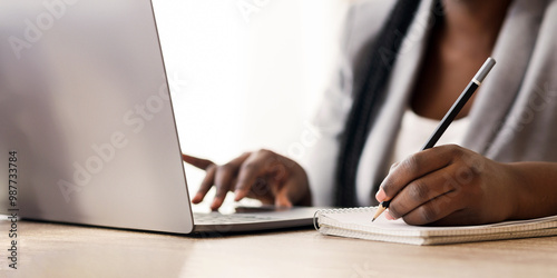 African american female entrepreneur working on laptop and taking notes in office, selective focus on hand with pencil, free space