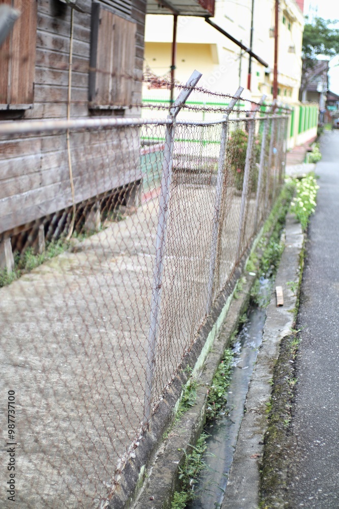 Chain-Link Fence with Barbed Wire Along Roadside in a Rural Community