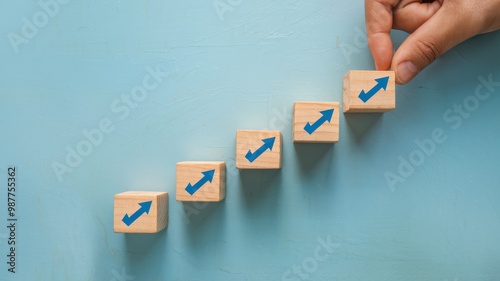 A light blue background contains a stair-like pattern of wooden blocks with upward-pointing arrows. The blocks represent growth, progress, or a step-by-step process.