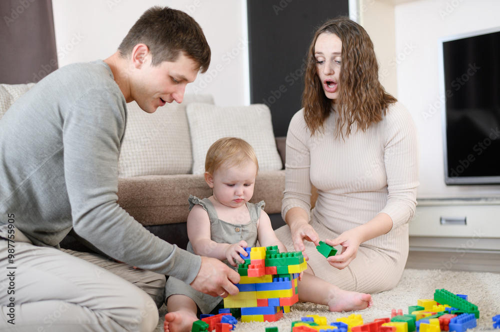 Leisure time together. Happy family, mom, dad and child enjoy at home, play with toy blocks, build building, sit at home on heated floor. Leisure time together. Happy family, mom, dad and child enjoy at home, play with toy blocks, build building, sit at home on heated floor.