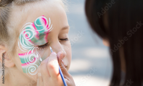 Baby face painting. Woman artist painting face of kid outdoors, copy space photo