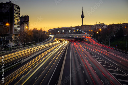 Traces of car lights at dusk driving along the Madrid ring road with the Piruli in the background