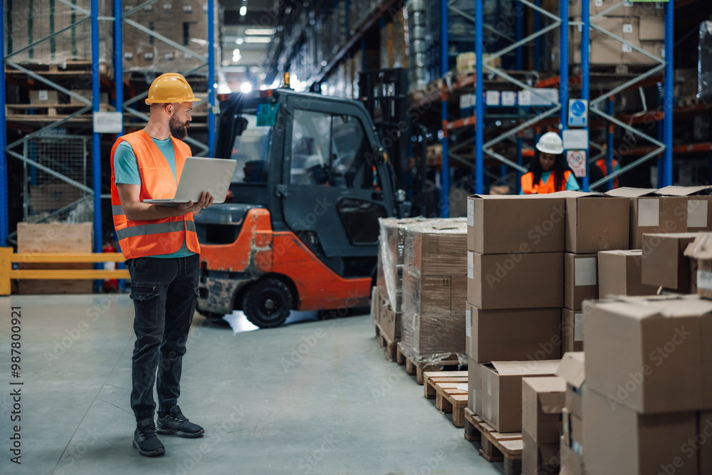 Fototapeta premium Warehouse worker using laptop to manage and track inventory levels.