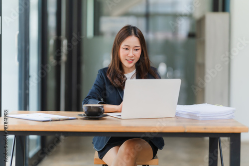 Focused Professional Grace: A young Asian businesswoman exudes confidence as she efficiently tackles her workload on a laptop, embodying modern workplace efficiency and ambition. 