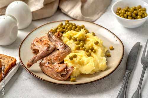 Pieces of rabbit stew, mashed potatoes and green peas on a plate on a bright table closeup