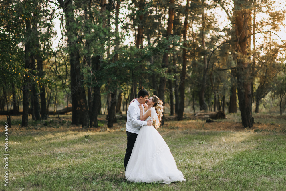 Fashionable groom and beautiful smiling bride curly blonde in white long dress hugging kissing outdoors in forest in nature evening at sunset. Wedding photography, portrait of happy newlyweds. Fashionable groom and beautiful smiling bride curly blonde in white long dress hugging kissing outdoors in forest in nature evening at sunset. Wedding photography, portrait of happy newlyweds.