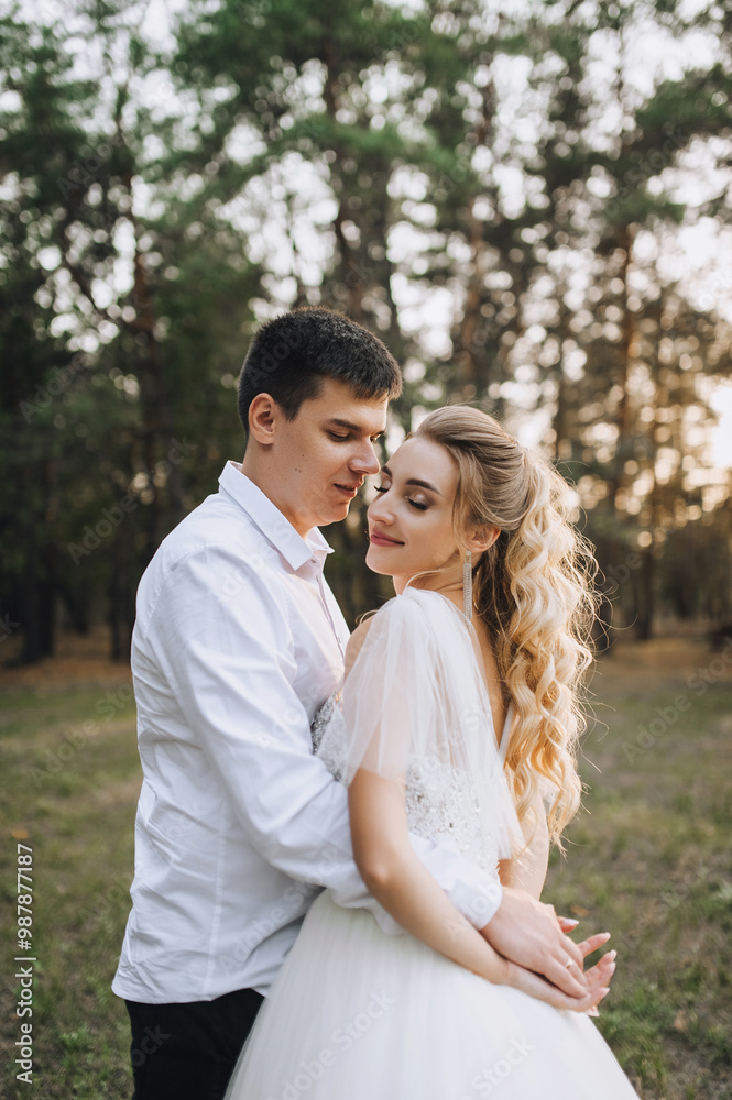 Young groom and beautiful smiling bride curly blonde in white lace long dress standing hugging outdoors in forest in nature at sunset. Wedding photography, portrait of happy newlyweds in love. Young groom and beautiful smiling bride curly blonde in white lace long dress standing hugging outdoors in forest in nature at sunset. Wedding photography, portrait of happy newlyweds in love.