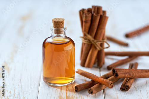 A bottle of essential cinnamon oil with cinnamon sticks on a white wooden table.