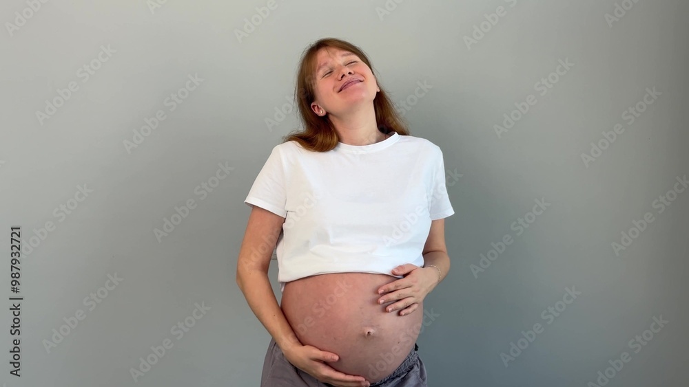 Happy young pregnant woman is stroking her belly isolated on grey background Happy young pregnant woman is stroking her belly isolated on grey background