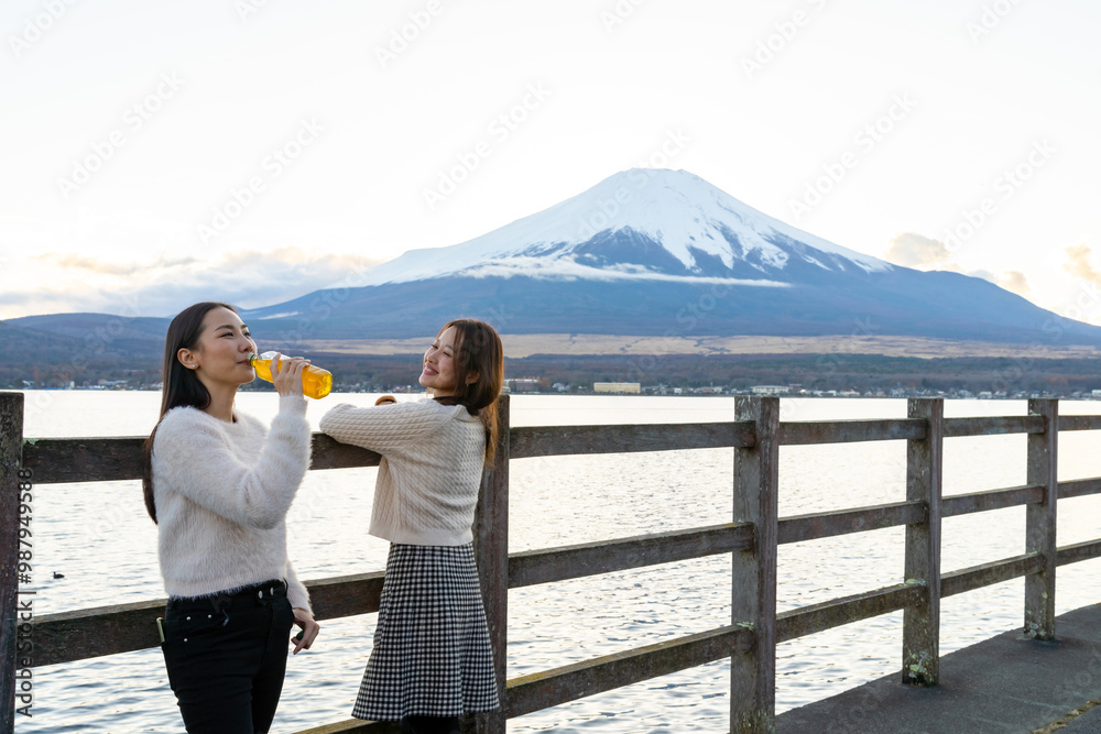 Happy Asian woman friend enjoy outdoor lifestyle travel nature in Japan on autumn holiday vacation. Attractive girl drinking tea from a bottle during travel Kawaguchi lake and Mount Fuji at sunset. Happy Asian woman friend enjoy outdoor lifestyle travel nature in Japan on autumn holiday vacation. Attractive girl drinking tea from a bottle during travel Kawaguchi lake and Mount Fuji at sunset.