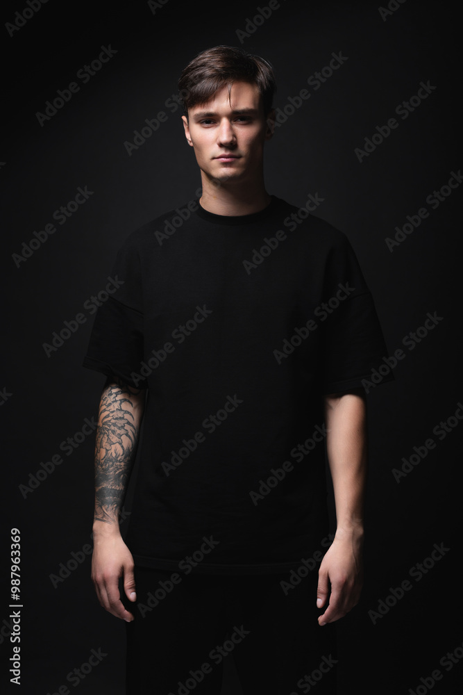 A guy of model appearance in black clothes poses on a black studio background. Male fashion portrait