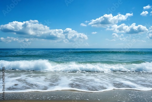 Blue Ocean Waves Crashing on Sandy Beach with White Clouds and Blue Sky