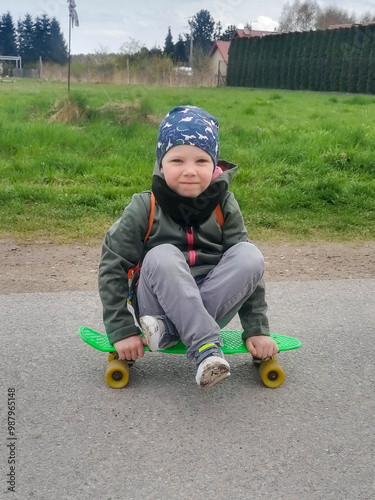 Little boy 4-5 years old wearing helmet and protecting his back is riding in sweater on mini skateboard on road down street. . High quality photo photo