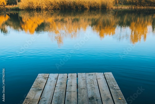 Wooden dock extending over tranquil blue lake water, reflecting fall foliage on opposite shore