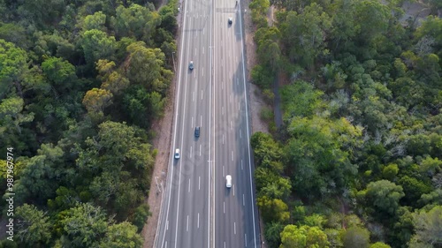Autoestrada em Monsanto, Lisboa, ao pôr do sol com tráfego em movimento. O céu alaranjado ilumina a estrada e os veículos, criando um contraste entre a natureza e a paisagem urbana.