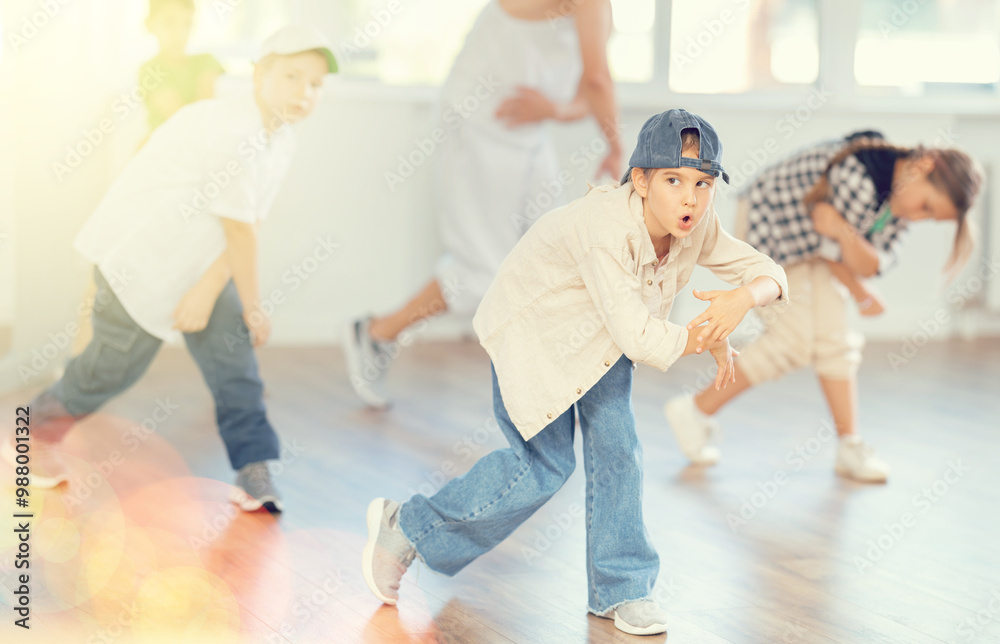 Fototapeta premium Young girl and group of positive children practicing energetic hip hop movements at modern dance school