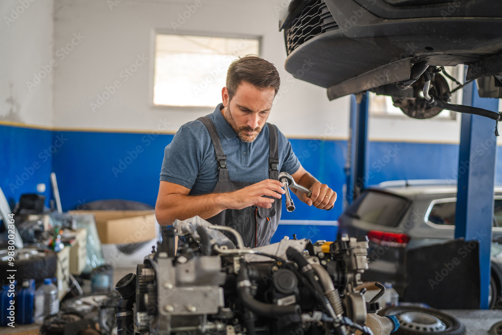 Car mechanic in navy overalls working on car engine with tools Car mechanic in navy overalls working on car engine with tools