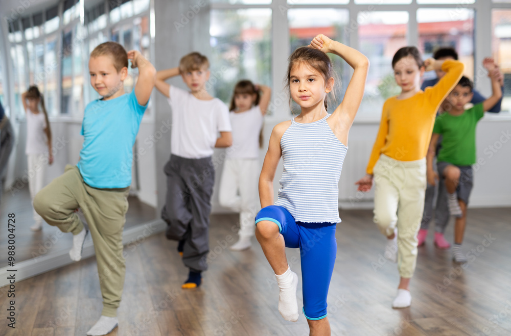 Fototapeta premium Active preteen girl practicing sport dances with other children and teacher during dancing classes