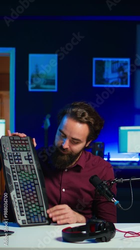 Vertical video Influencer in studio reviewing gaming keyboard, mouse and headphones. Online show host filming electronics haul, presenting wired computer peripherals to viewers during live broadcast photo