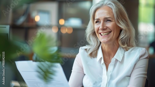 Smiling mature business woman hr holding cv document at job interview. Happy mid aged professional banking manager or lawyer consulting client sitting at workplace in corporate office meeting.