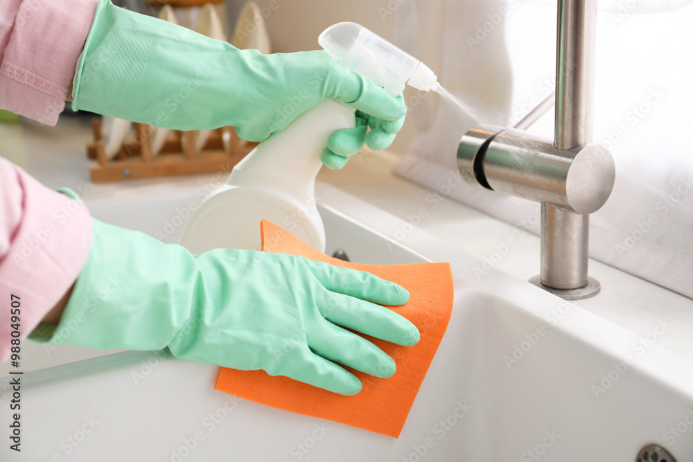 Woman with spray bottle of detergent and napkin cleaning tap in kitchen, closeup Woman with spray bottle of detergent and napkin cleaning tap in kitchen, closeup