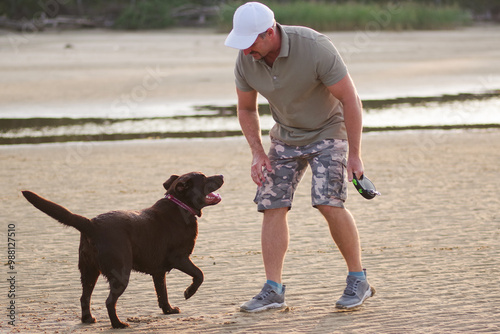 45-year-old Caucasian man plays with a chocolate Labrador retriever on the beach at sunset. people and pets. photo