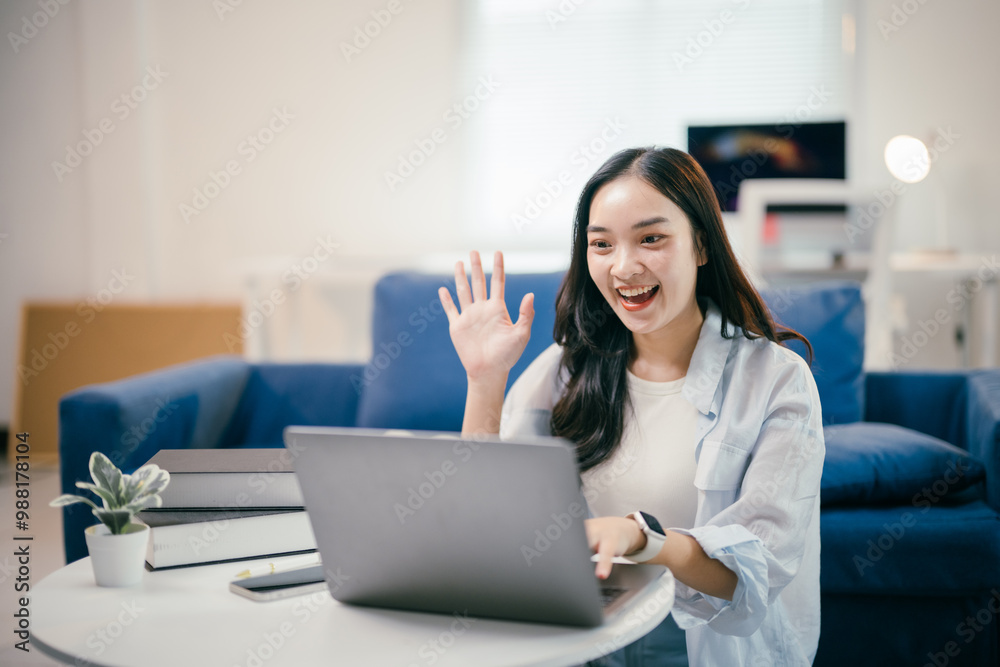 Cheerful freelancer is waving hello while participating in a video conference on a laptop, working remotely from her home office Cheerful freelancer is waving hello while participating in a video conference on a laptop, working remotely from her home office
