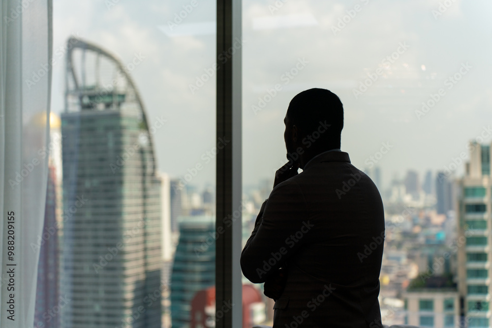 Silhouette of a Black Businessman By the Windows Overlooking the Cityscape Silhouette of a Black Businessman By the Windows Overlooking the Cityscape