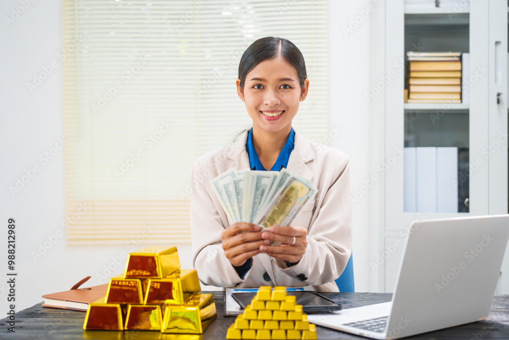 An Asian businesswoman is sitting at her desk, discussing gold bars, deposits,and the gold market with investors.She analyzes gold price trends highlights the long-term benefits of investing in gold An Asian businesswoman is sitting at her desk, discussing gold bars, deposits,and the gold market with investors.She analyzes gold price trends highlights the long-term benefits of investing in gold