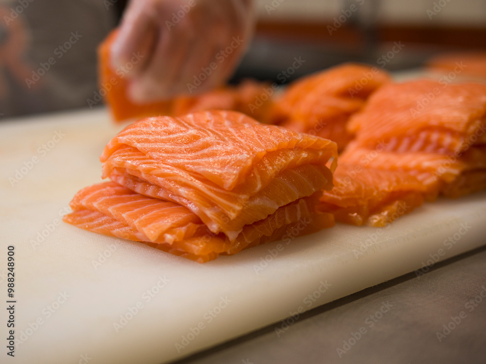 A master chef expertly slices fresh salmon into uniform pieces. With gloved hands and a special knife, he ensures each portion of salmon is evenly cut, maintaining the natural texture of salmon. A master chef expertly slices fresh salmon into uniform pieces. With gloved hands and a special knife, he ensures each portion of salmon is evenly cut, maintaining the natural texture of salmon.