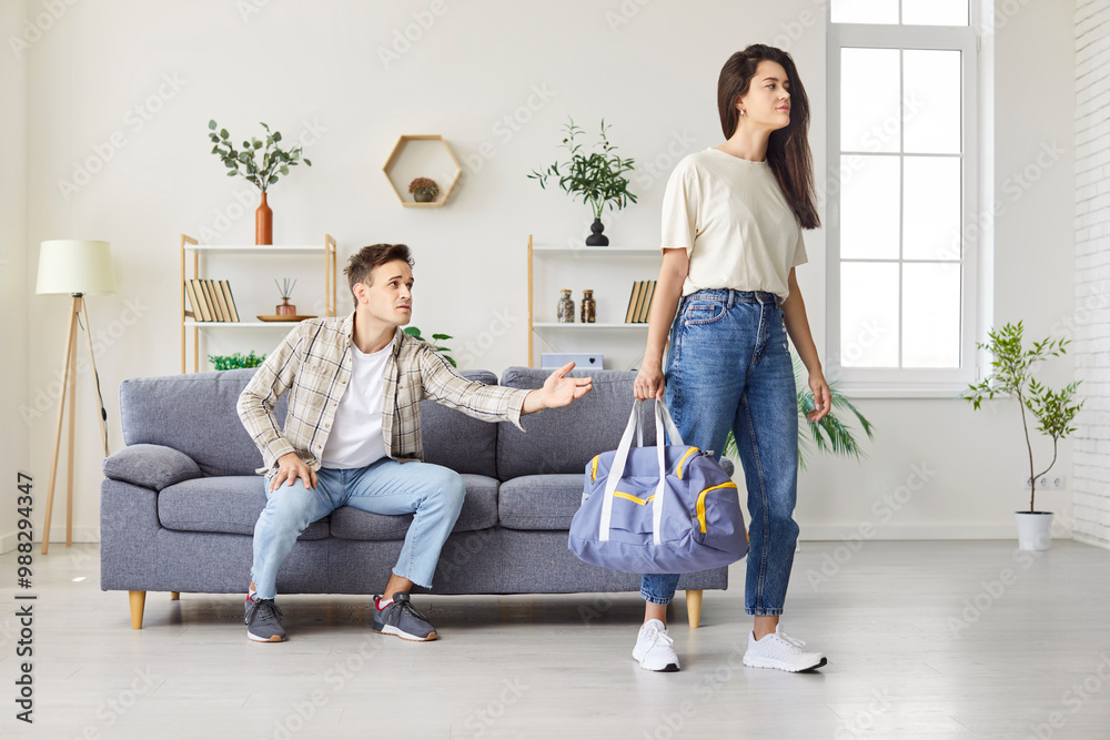 Sad wife with bag walking away from husband during a conflict or divorce at home living room. Negative motions of breakup, bad family relationships, and domestic quarrels into couples. Sad wife with bag walking away from husband during a conflict or divorce at home living room. Negative motions of breakup, bad family relationships, and domestic quarrels into couples.