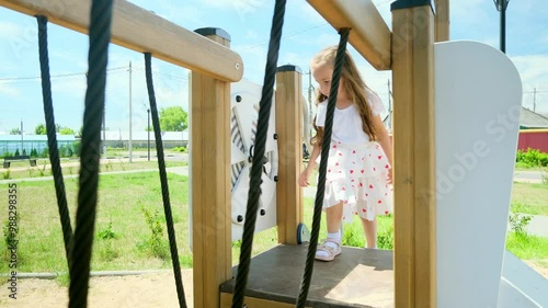 4k footage of funny toddler girl climbing on wooden stapladder on children playground at park photo