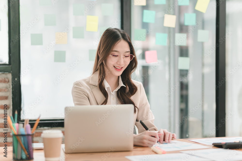 A smiling woman sits at a desk with a laptop, surrounded by colorful sticky notes and office supplies, conveying a productive work atmosphere. A smiling woman sits at a desk with a laptop, surrounded by colorful sticky notes and office supplies, conveying a productive work atmosphere.
