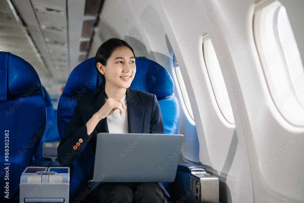 Asian businesswoman or entrepreneur in a formal suit on an airplane sitting in business class using a phone, computer laptop. Travel in style, work