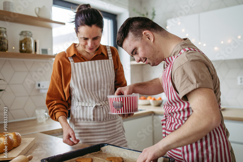 Young man with Down syndrome and his mom baking Christmas gingerbread cookies. Christmas peaceful moment for man with Down syndrome. photo